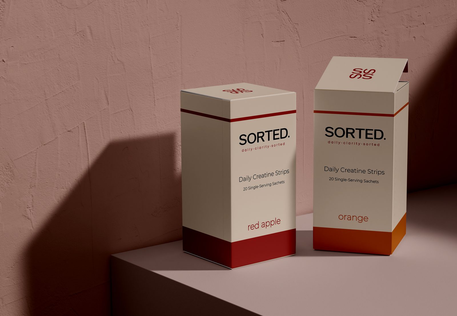 Two cream SORTED. Daily Creatine Strips boxes, one in red apple and one in orange, against a soft pink wall